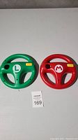 Front view of red and green Mario Kart steering wheel attachments showing logos and button details.
