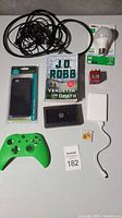 Full lot shown including green Xbox controller, iPhone case, cables, game cartridge, book, adapters, and charger.