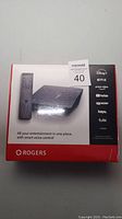 Factory sealed Rogers Entertainment Box with remote control, showcasing front packaging displaying logos for supported streaming services and smart voice control feature.