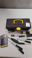 Closed black and yellow plastic toolbox with various screwdrivers and bits laid around it on a flat surface