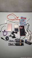 Full lot overview photo showing all items on a plain surface including cables, charging blocks, phone cases, batteries, and other small electronics.