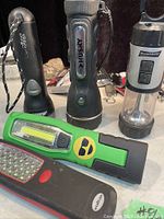 Photo shows a group of five flashlights of various makes and styles placed upright on a surface.