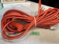 Coiled orange 50 foot extension cord with 3-prong plug and socket ends placed on table.