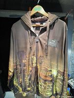 Front view of the men's XL brown hoodie with cityscape design on lower half, zipper front and hood with drawstrings.