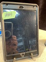 Front view of Apple iPad with screen smudges and dirt visible, black OtterBox case partially visible