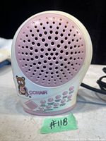 Front view of white and pink Conair Cuddle Pals sound machine with speaker grill and bear graphic.
