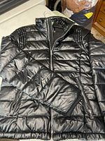 Black Guess winter jacket laid out to show full front and sleeve detail, showing the quilted pattern, high collar, and zippered pockets.