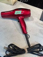Red Babyliss Pro hair dryer lying flat on a table with attached power cord coiled neatly beside it.