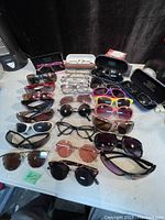 Overview of all glasses in lot showing multiple pairs of sunglasses and reading glasses including cases.