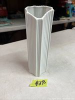 White porcelain vase with fluted triangular shape on a table, showing front and side detail.