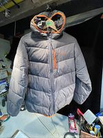 Front view of the gray Columbia winter jacket with an orange trimmed hood hanging on a hanger in a basement or workshop setting.