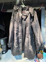 Front view of long waterproof ladies jacket with hood and multiple pockets hung on a hanger.