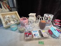 Overview of all items on a flat surface showing electric Scentsy warmers, decorative candle holders, boxed wax melts, and individual wax melts in packaging.