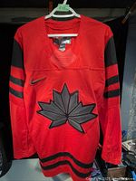 Front view of red hockey jersey with black maple leaf and black stripes on sleeves and hem.