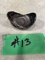 Front view of rare antique silver Chinese Sycee coin, showing stamped Chinese characters and a concave boat-like shape.