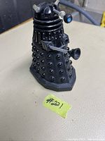 Front and side view of black Dalek toy showing studded body, arms, and head with antennae.