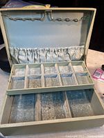 Open view displaying the inside of the vintage jewellery box lined in light blue velvet fabric. Features a top tray with 10 compartments and a larger base section divided into 3 compartments. The lid interior has a fabric pouch pocket and slots for hanging jewellery.