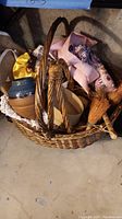 Photo showing the wicker basket filled with multiple household items including a ceramic vase, cloths, and a broom.