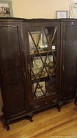 Front view of antique wooden cabinet showing the glass display door with X-shaped wooden overlays and solid wood side doors.