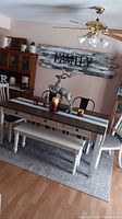 Full view of dining table, chairs, bench and area rug in room with wall decoration and ceiling fan