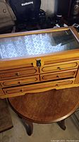 Closed view of the wooden display box showing glass lid and four small drawers on front.