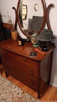 Full view of the antique wooden dresser with attached large oval mirror and wooden curved supports. Shows three drawers with round wooden knobs. Items on dresser visible but not included.