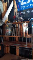 Wooden hanging shelf mounted on wall with fishing poles and metal Exide Batteries sign visible in background, also large metal Watco oil finish can on shelf
