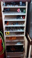 Wooden shelving with items organized by shelf including batteries, tape, hand tools, and hardware.