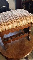 Close-up image of the padded ottoman seat with striped upholstery and studded edges on a wooden base.