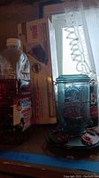 Photo showing boxed handheld vacuum cleaner, glass hummingbird feeder, and hummingbird nectar bottle together on shelf