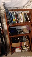 Wooden collapsible shelf unit with books on top shelf, assorted smaller items on middle shelf and boxes on bottom shelf