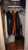 Closet with hanging jackets, white hangers, and a wooden chair inside.