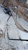 Outdoor portable net hammock with metal frame standing in snow-covered yard, showing hammock spreader bars and black metal base.