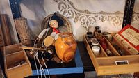 Wide view of shelf with mixed vintage collectibles, marionette puppet, pottery, tools and boxes