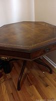 Full view of vintage octagonal wooden table with brown leather top showing wear and gold embossed edge.