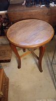 Front-angle view of a round solid wood accent table with four curved legs and cross support