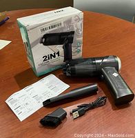 Black 2-in-1 cordless handheld vacuum cleaner with detachable brush nozzle, USB charging cable, instruction manual, and retail box on wooden surface.