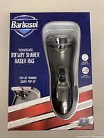 Front view of the boxed Barbasol rechargeable rotary shaver with visible rotary head through plastic window and pop-up trimmer image on packaging.