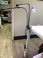 LED grow light attached to the edge of a white table by a clamp, showing three flexible arms with LED light shades illuminated.