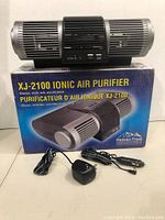 Black cylindrical Heaven Fresh XJ-2100UV ionic air purifier with two adapters placed in front of the retail box featuring product image and branding.