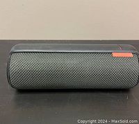 Front view of Logitech UE Boom Bluetooth speaker showing indigo fabric mesh and orange rubber strip with button controls.