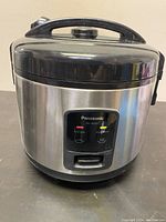 Front view of Panasonic SR-JN105 electric rice cooker showing stainless steel body with Panasonic label, control panel with red and yellow indicator lights.