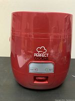 Front view of small red electric rice cooker with Perfect Cooker logo and cook/warm indicator lights.