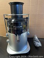 Front view of PowerXL SHL96 juicer with power cord beside it showing the spout.
