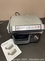 Front angle view of T-FAL Super Grill closed with control dial and manual placed in front.