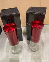 Two red Wolfgang Puck electric spice mills with metallic tops, clear acrylic chambers, and black original packaging boxes behind them.