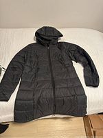 Full view of black hooded puffer jacket laid flat showing front, sleeves, attached hood and zipper.