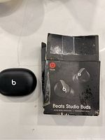 Black Beats Studio Buds earbuds with charging case alongside original box showing wear and tear.