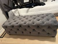 Side view showing the overall rectangular shape, deep button tufting on sides and top, soft velour-like gray fabric, and low black legs.