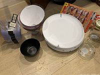 Photo shows clear glass mixing bowl, black plastic bowl, white plastic plates, spice cabinet magnets, and candle holder on floor.